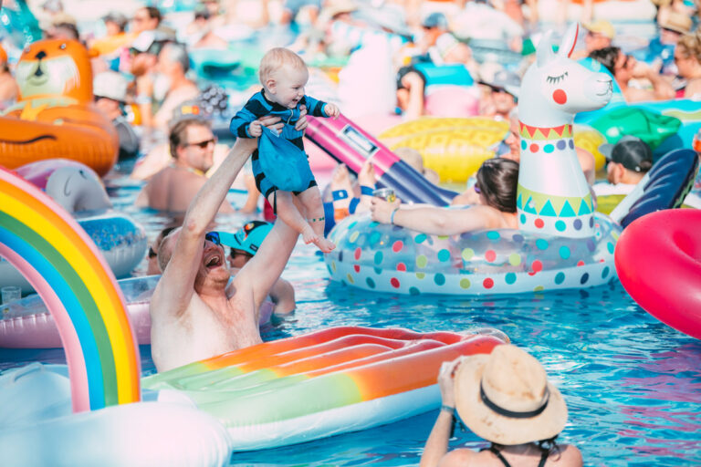 A guest holding up their baby above their head in the pool.