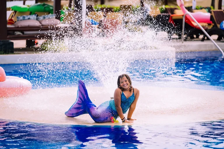 Guest in a mermaid costume posing on a fountain in the middle of the main pool