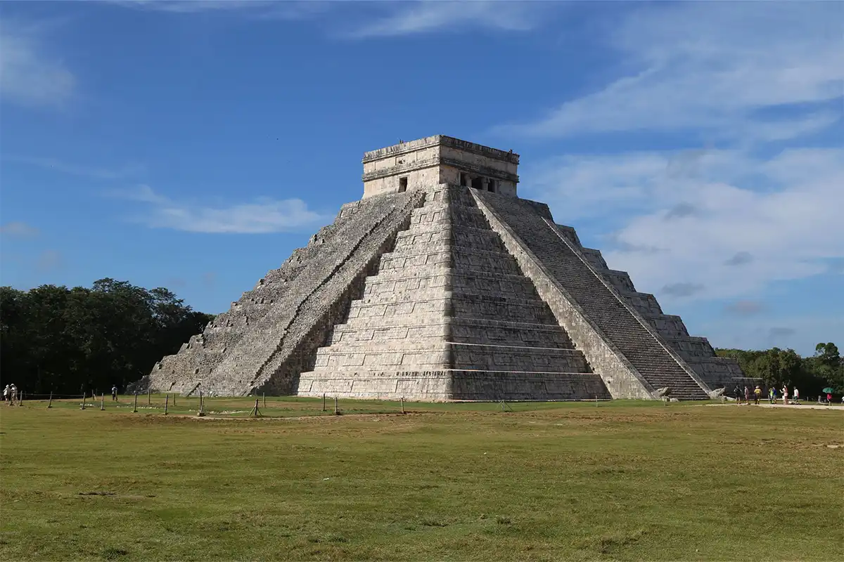 A mayan temple sits in the middle of a grass field.