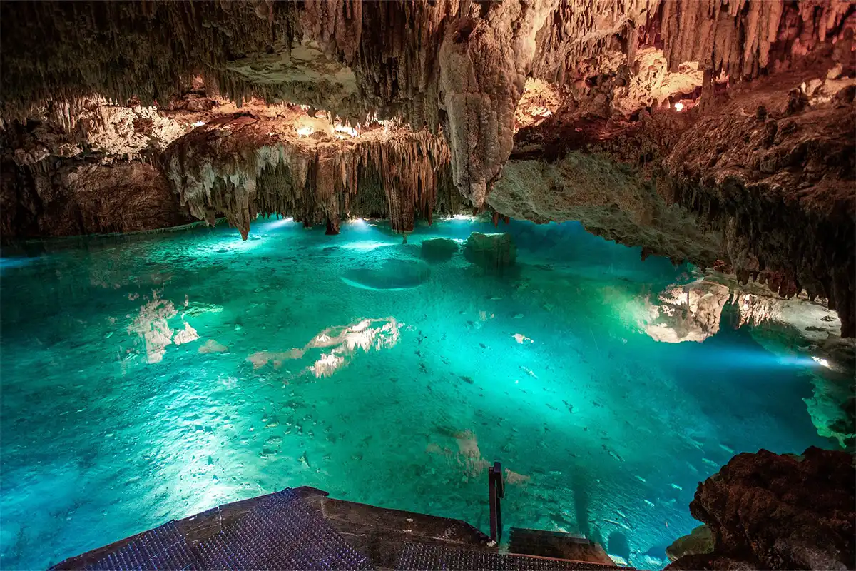 An underground cenote, clear blue water lit up by underwater lights.