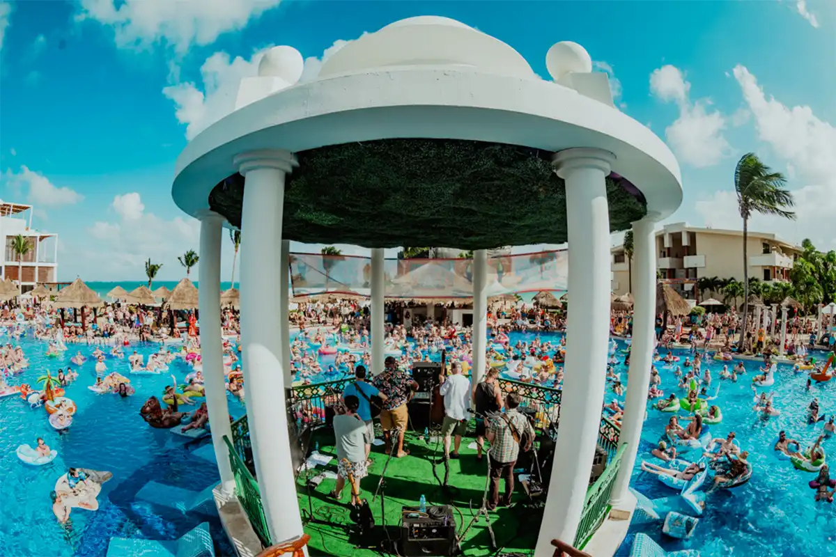 Band performing on pool gazebo stage with guests floating in the pool watching.