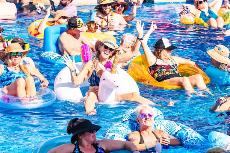 A guest sitting on a unicorn pool float with their hands up.