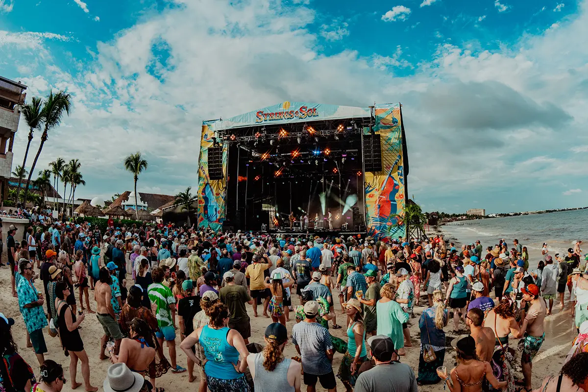Daytime Beach Stage concert with crowd dancing in the sand.