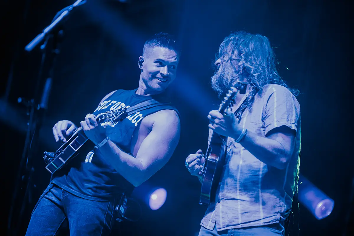 Nick Piccinni and Paul Hoffman performing together on stage under blue light.