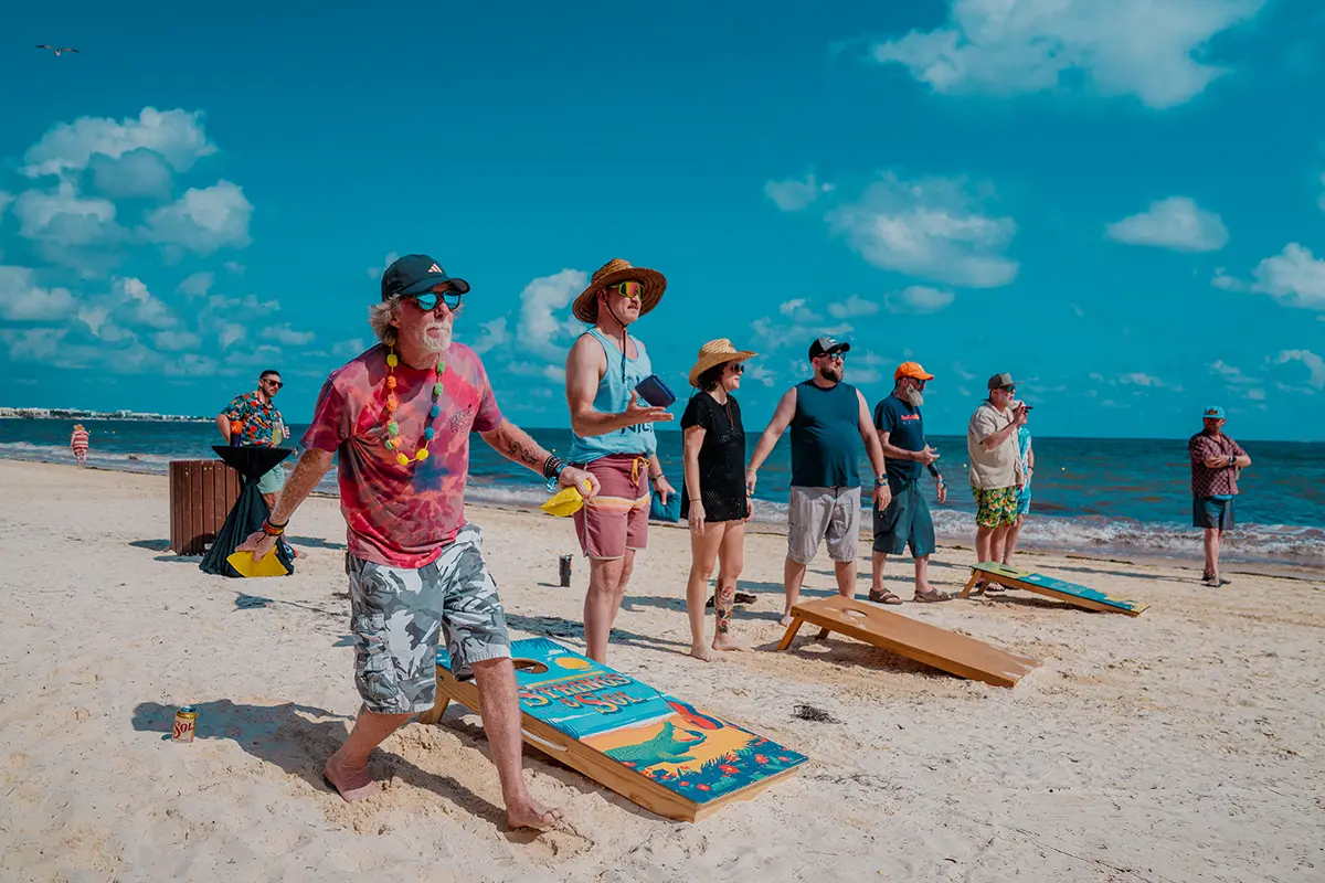 Guests playing cornhole on the beach during daytime with ocean in the background.