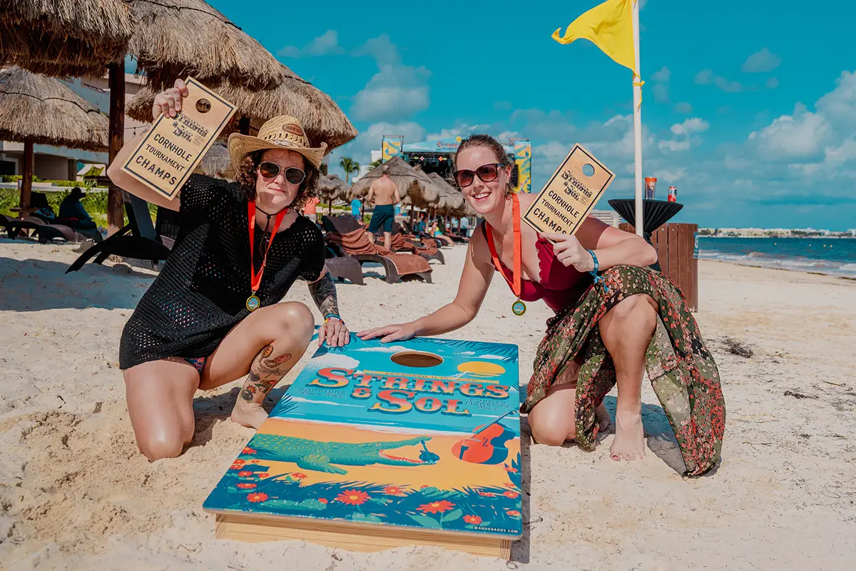 Guests holding up cornhole tournament trophies on the beach.